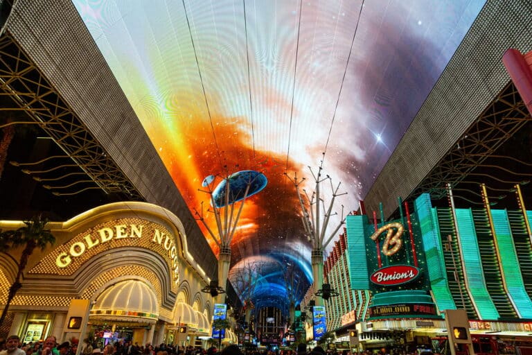 a view of the Viva Vision Light Show on the canopy of Fremont Street. The Golden Nugget Casino is also pictured, along with a crowd underneath the canopy and zipline.