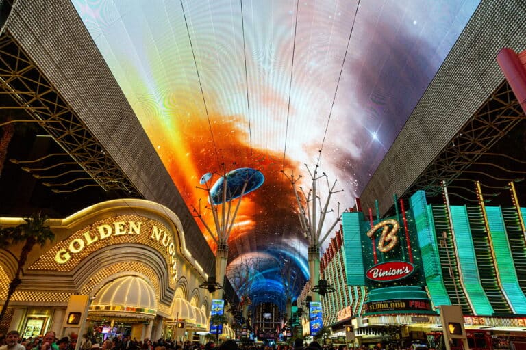 A view of the viva vision light show on the canopy of fremont street. The golden nugget casino is also pictured, along with a crowd underneath the canopy and zipline.