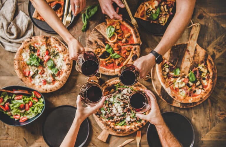 Dining in downtown Las Vegas. An aerial view of a variety of pizzas as friends make a toast with their wine glasses above it.