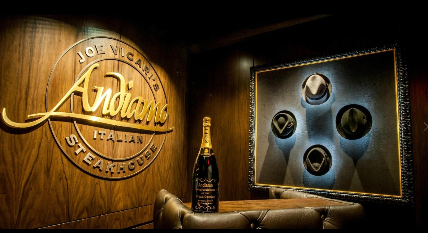 The sign for Andiamo Steakhouse at the D, along with a bottle of champagne and four hats hanging on the wall.